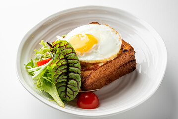Toasted sandwich with sunny-side-up egg and fresh salad on white plate. Minimalist food presentation, top view, isolated on white background.