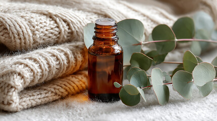 Amber essential oil bottle placed on soft knit fabric next to fresh eucalyptus leaves, natural wellness and aromatherapy concept, warm and cozy atmosphere