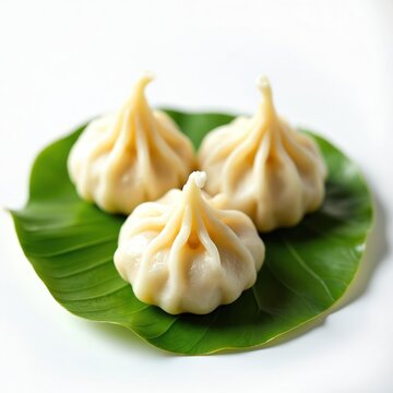 Three modak dumplings on green leaf against white background. Steamed modak, traditional Indian sweet dessert. Modak on banana leaf. Freshly cooked modak for Hindu festival. Modak for Ganesh