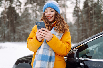 Portrait of happy woman in a bright jacket taking selfie while standing next to car on winter day....
