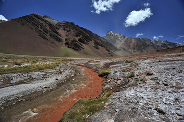 A small river flowing through a valley between mountains. A muddy mountain river flowing through a rocky gorge