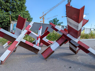 Anti-tank hedgehogs painted in red and white stripes. Military barriers on the way asphalt of city streets. Echoes of war in neighborhoods and street intersections.