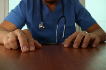 Doctor in scrubs with stethoscope resting hands on desk
