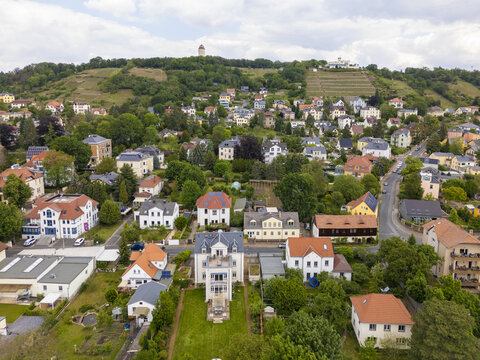 Aerial view of quaint red-roofed houses nestled among verdant trees, leading up to the distant Spitzhaus and Belvedere, Radebeul, Saxony, Germany.