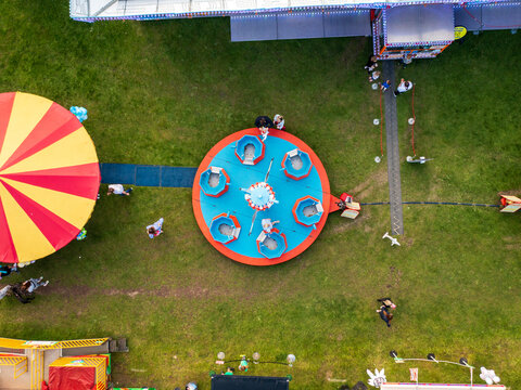 Aerial view of a vibrant fairground scene, with a spinning ride and a colorful canopy against a backdrop of green grass, Hook, England, United Kingdom.