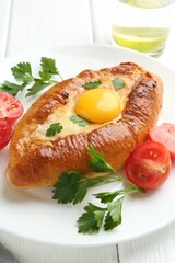 Tasty khachapuri with cheese, egg, tomatoes and parsley on white wooden table, closeup