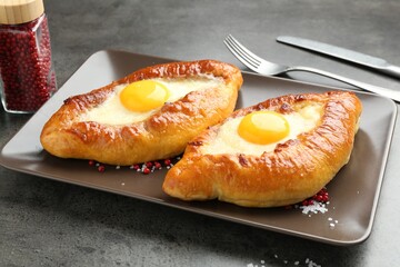 Tasty khachapuris with cheese and eggs served on grey table, closeup