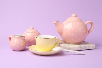 Beautiful ceramic tea set for children on violet background, closeup