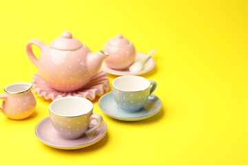 Beautiful ceramic tea set for children on yellow background, closeup. Space for text