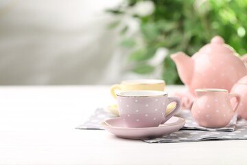 Beautiful ceramic tea set for children on white wooden table against blurred background, closeup. Space for text