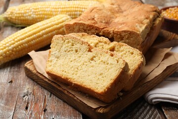 Freshly baked cut cornbread and cobs on wooden table, closeup