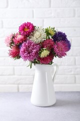 Beautiful flowers in vase on grey table near white brick wall indoors