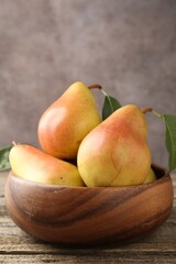 Fresh ripe pears with green leaves in bowl on wooden table, closeup