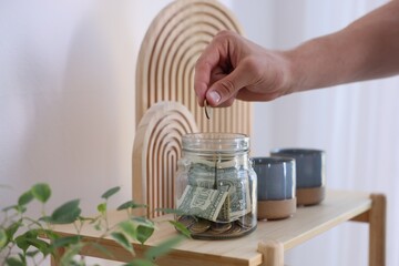 Man putting money into jar at wooden table indoors, closeup