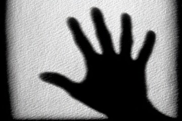 A dark hand shadow silhouetted against a textured white surface, dramatic lighting