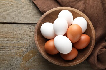 Fresh chicken eggs in bowl on wooden table, top view. Space for text
