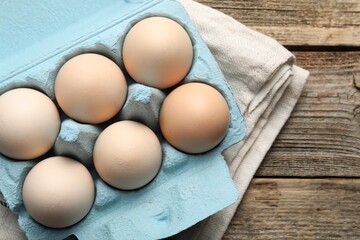 Raw chicken eggs in egg carton on wooden table, top view. Space for text