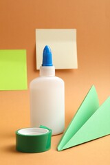 Glue, adhesive tape and paper plane on pale orange background
