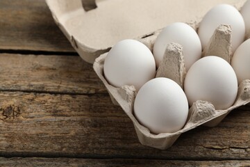 Raw chicken eggs in egg carton on wooden table, closeup. Space for text