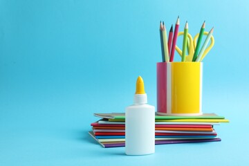 Obraz premium Glue in bottle, notebooks, color pencils and scissors on light blue background, closeup. Space for text