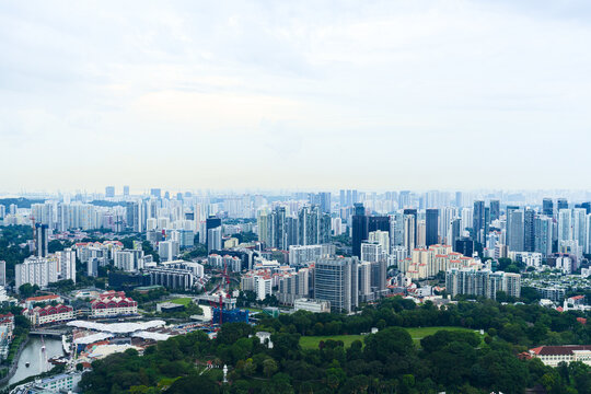 Aerial view of a modern cityscape where high-rise buildings meet lush greenery under a soft, diffused sky, Singapore, Singapore.