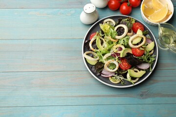 Delicious salad with squid rings and ingredients on light blue wooden table, flat lay. Space for text