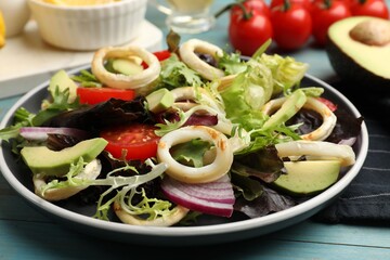 Delicious salad with squid rings and ingredients on light blue wooden table, closeup