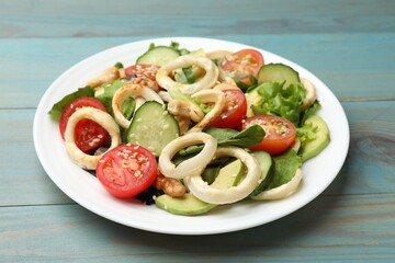Delicious salad with squid rings, avocado, nuts and vegetables on light blue wooden table, closeup