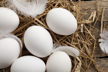 Raw chicken eggs, feathers and straw on wooden table, flat lay
