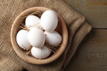 Raw chicken eggs and straw in bowl on wooden table, top view. Space for text
