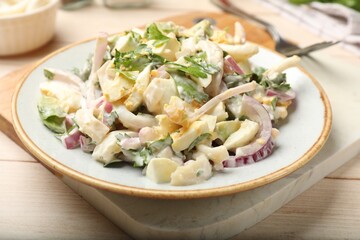 Tasty salad with squid rings, onion and eggs served on light wooden table, closeup