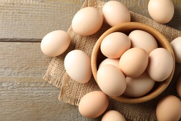 Raw chicken eggs in bowl on wooden table, flat lay. Space for text