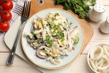 Tasty salad with squid rings, onion and eggs served on light wooden table, flat lay