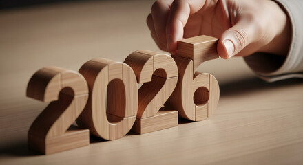 Woman hand placing wooden block to form 2026. Setting new year goals and future planning. Conceptual illustration for success.