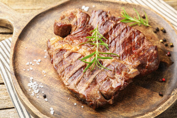 Delicious grilled beef steak with rosemary, salt and peppercorns on wooden table, closeup