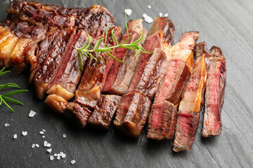 Pieces of delicious grilled beef steak with rosemary and salt on grey textured table, closeup