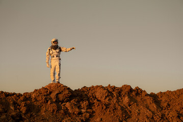 Astronaut in spacesuit exploring alien terrain and stretching hand toward the horizon.
