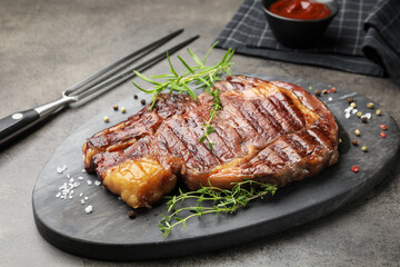 Delicious grilled beef steak with herbs, spices and carving fork on grey textured table, closeup
