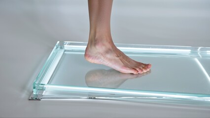 A Human Foot Standing on a Reflective Glass Surface with Subtle Lighting