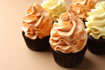 Delicious cupcakes with colorful cream on beige background, closeup