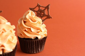 Delicious cupcakes with chocolate web on coral background, closeup with space for text. Halloween celebration