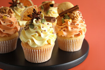 Delicious cupcakes with sprinkles, cookies, spices and dry orange slices on stand against coral background, closeup. Autumn atmosphere