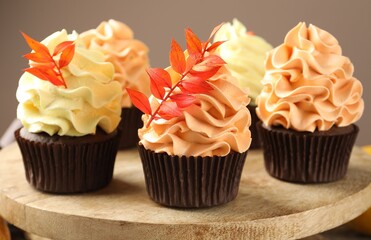 Delicious cupcakes with branches with red leaves on stand against grey background, closeup. Autumn atmosphere