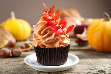 Delicious cupcake with branch with red leaves on wooden table against grey background, closeup. Autumn atmosphere