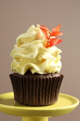 Delicious cupcake with branch with red leaves on stand against grey background, closeup. Autumn atmosphere