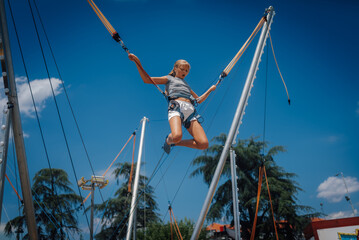 Girl bouncing on bungee trampoline having fun in amusement park