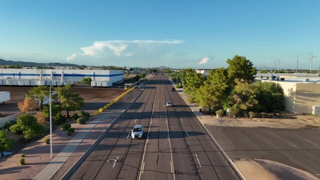 Static Shot of Cars driving down Empty Road with trees on one side and buildings on other side, late afternoon, North 56th Street in Chandler Arizona, Camelback Mountain in the far background