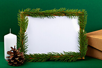 Fototapeta premium Mockup. Christmas. Blank photo frame mockup for design or advertising adorned with fresh pine branches, accompanied by white candle and pine cone, set against vibrant green background
