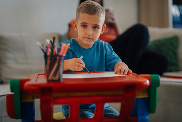 Child drawing on paper at home with colorful markers and pencils