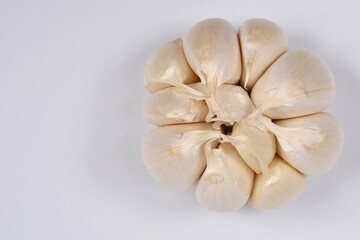 A close-up, centered, overhead studio shot displays garlic bulb with unpeeled cluster of garlic cloves against a white background